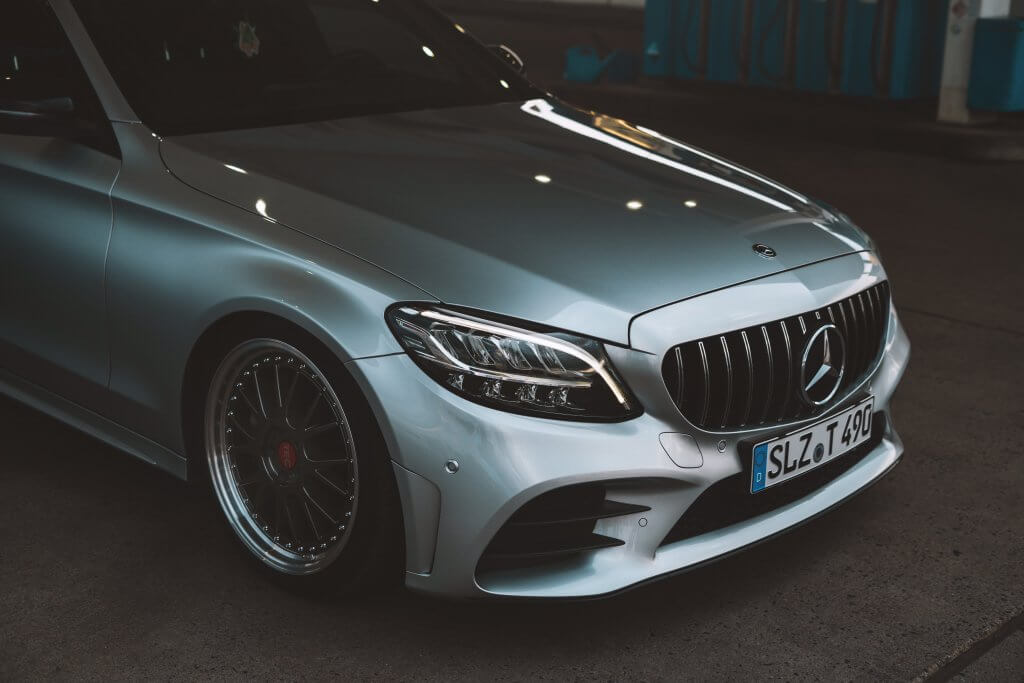 Ein silberner Mercedes-Benz steht auf dem Asphalt, Scheinwerfer leuchten, deutsches Kennzeichen gut zu erkennen