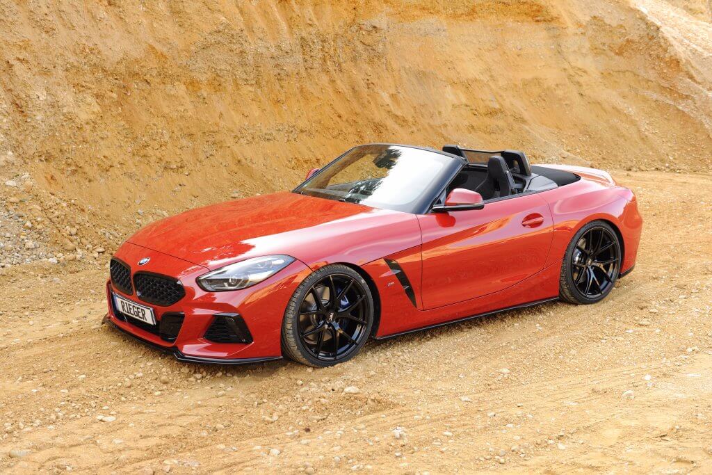 Ein roter BMW Cabrio-Sportwagen parkt auf einem Feldweg vor einer sandigen, felsigen Böschung