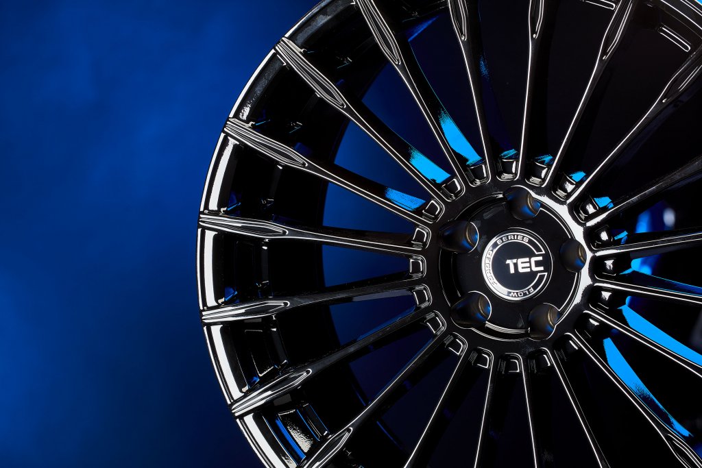 Glänzende schwarze Alufelge mit mehreren Speichen vor blauem Farbverlauf im Detail