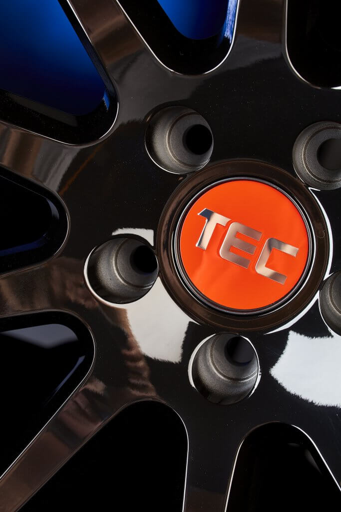 Nahaufnahme einer glänzend schwarzen Autofelge mit orangefarbener Nabenkappe, auf der silbern TEC steht