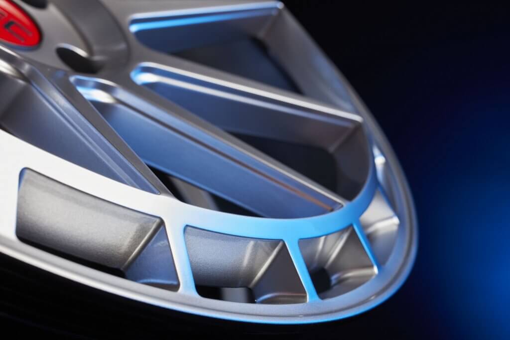 Nahaufnahme einer silbernen, metallischen Autofelge mit modernem, kantigem Design vor dunkelblauem Hintergrund