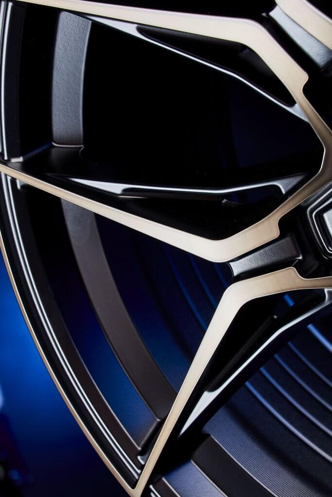 Nahaufnahme einer schwarzen und silbernen Alufelge mit scharfen, kantigen Speichen vor blauem Hintergrund