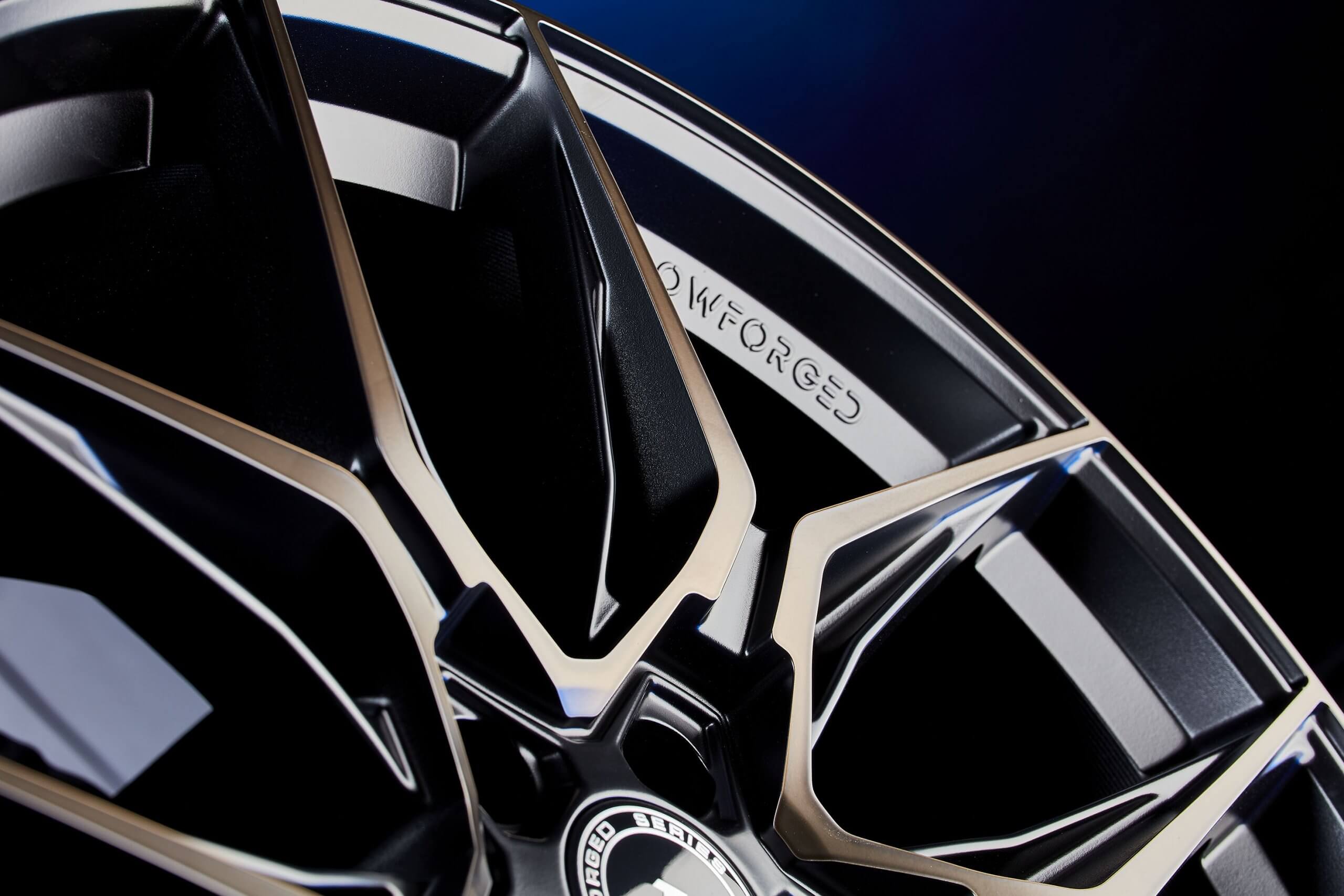 Nahaufnahme einer schwarz-silbernen FLOWFORGED-Alufelge mit filigranem, kantigem Speichendesign und Gravur auf dem Rand