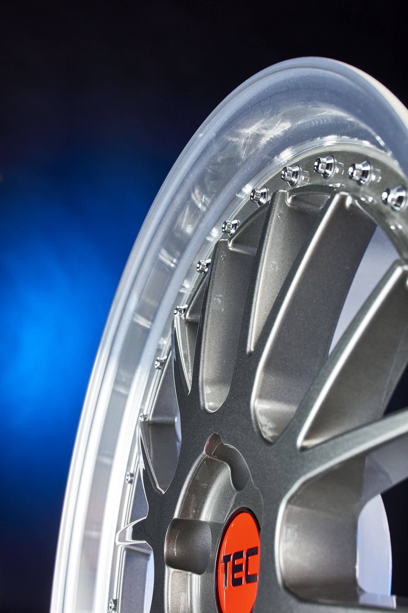 Nahaufnahme einer silbernen Alufelge mit roter Nabenkappe vor blau-schwarzem Farbverlauf