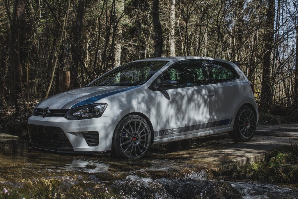 Ein weißer VW-Kompaktwagen steht auf einem kleinen Bach in einem Wald, durch dessen Bäume Sonnenlicht fällt