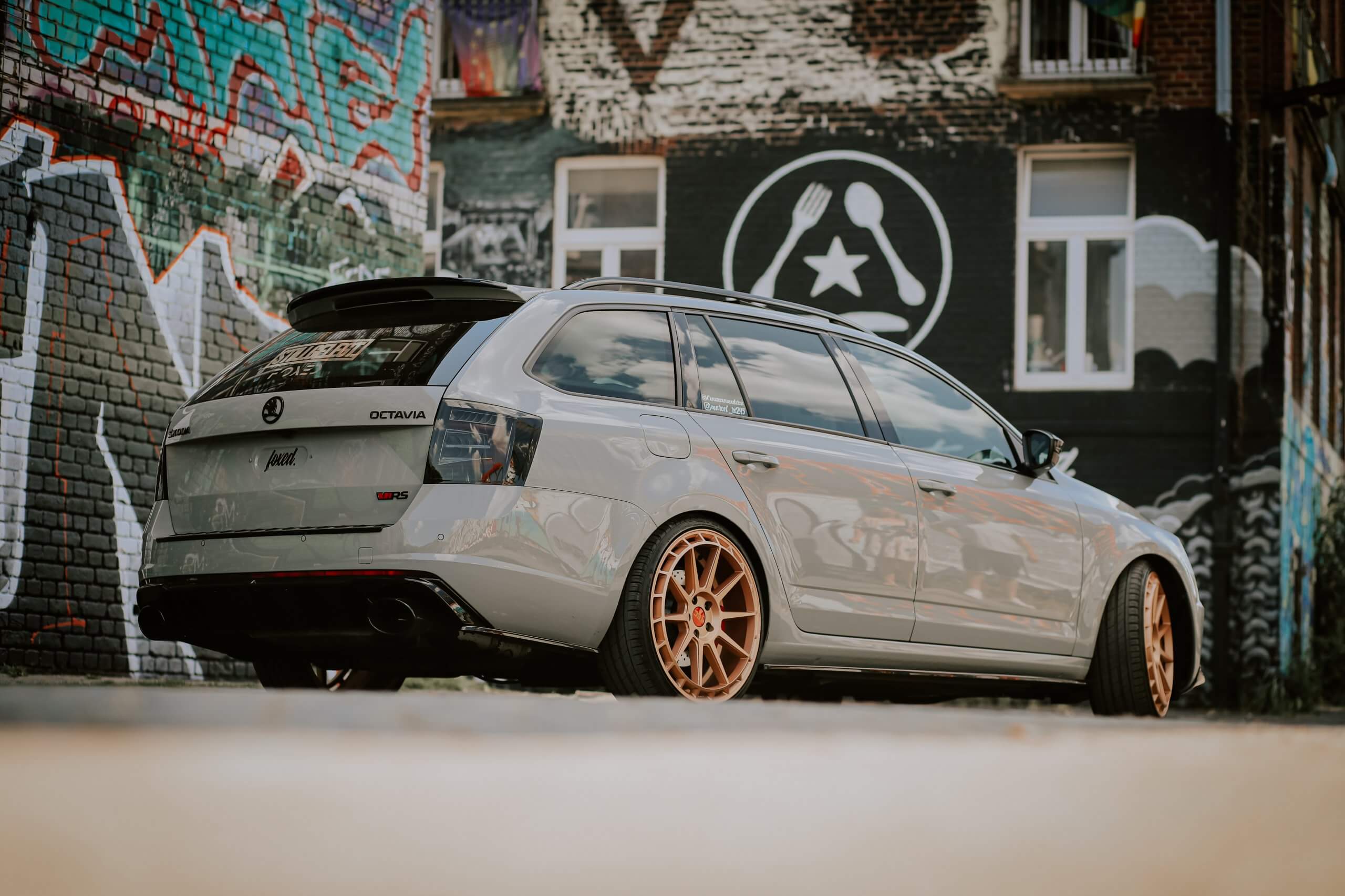 Ein silberner Skoda Octavia Kombi mit bronzefarbenen Felgen parkt vor einer von Graffiti bedeckten Wand mit stilisiertem Wandbild im Hintergrund