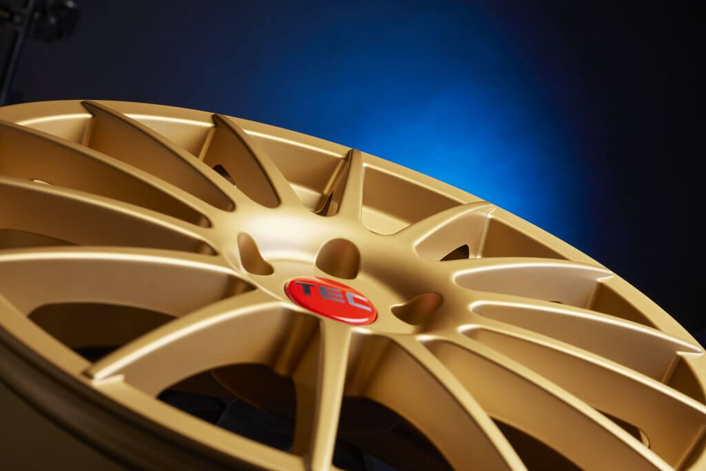Nahaufnahme einer goldenen TEC-Alufelge mit roter Nabenkappe vor blau-schwarzem Farbverlauf