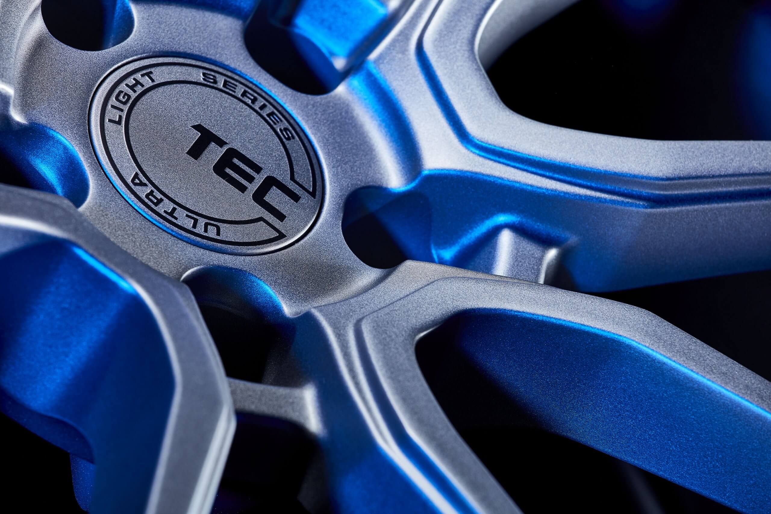 Nahaufnahme einer metallic-blauen und silbernen TEC Ultra Light Series Flowforged Felge mit feiner Struktur und GT Race Logo in der Mitte