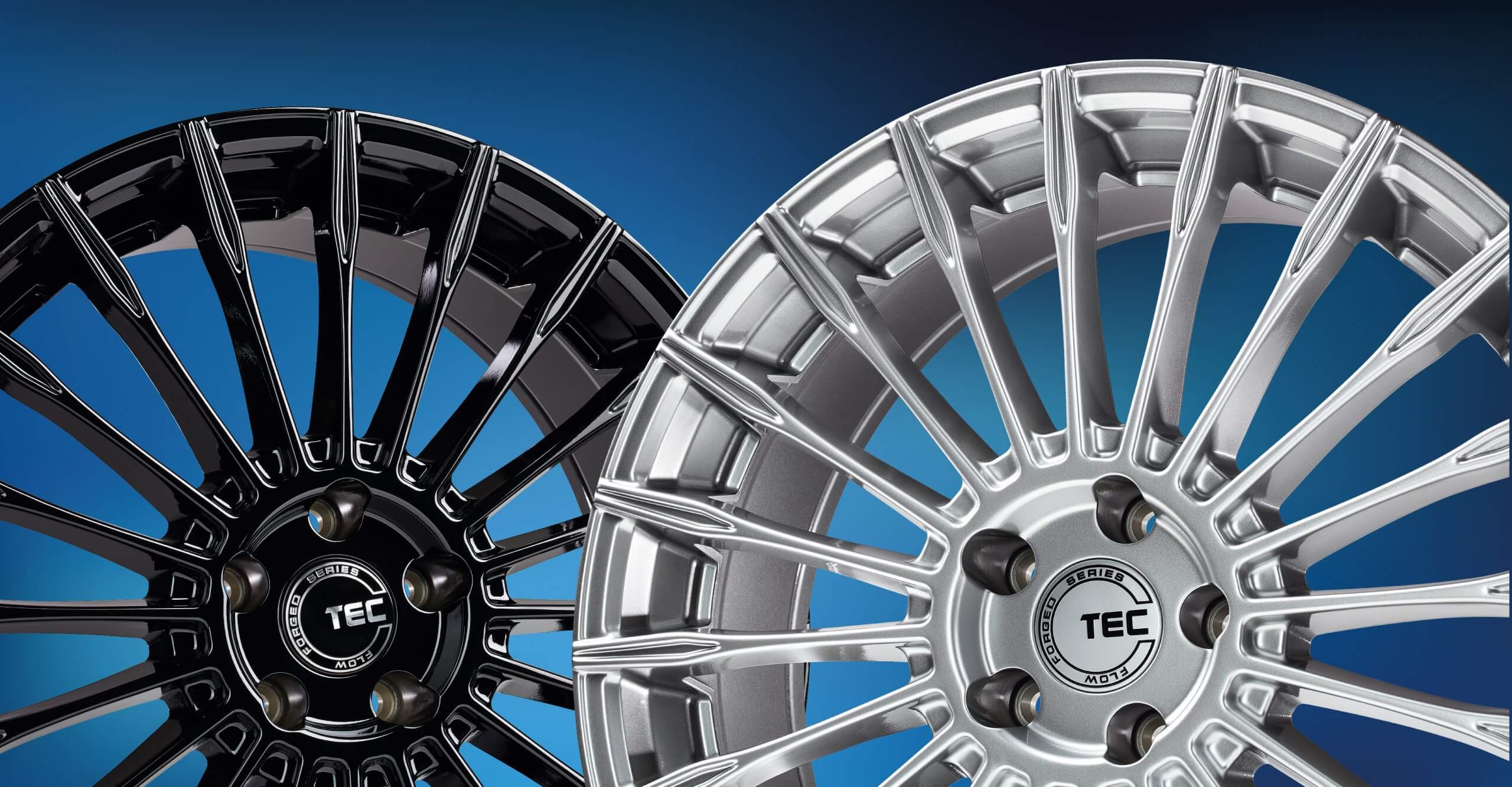 Zwei Alufelgen mit Speichendesign und TEC-Logo, eine glänzend schwarz, eine silberfarben, liegen nebeneinander auf blauem Hintergrund